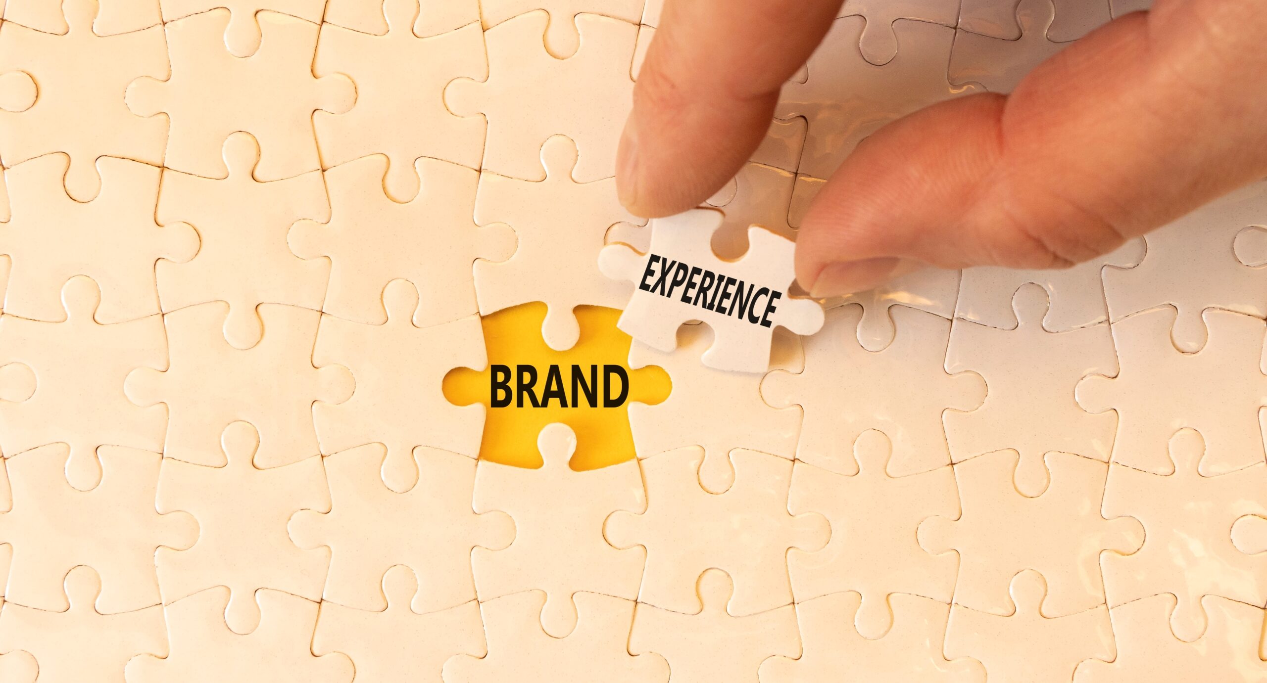 A hand completes the puzzle by joining “BRAND” and “EXPERIENCE” pieces.