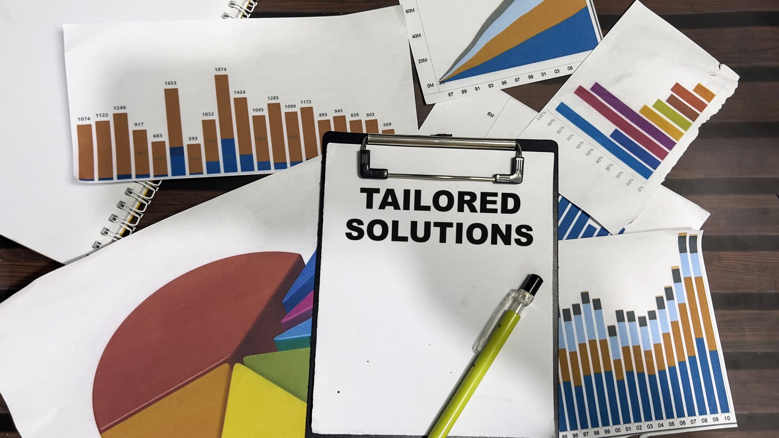 "Tailored Solutions" text-written on a paper with graphs and charts behind.